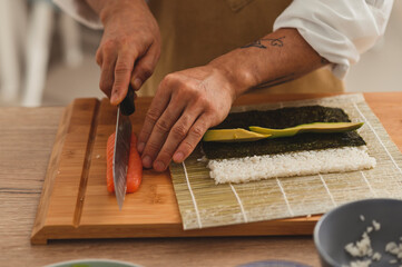 Close up preparing roll sushi at home. Male hands slicing ingredients salmon, cucumber, avocado and cream cheese