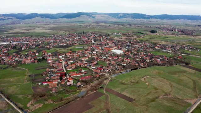 Aerial forward tilt down over Sansimion village and Ciuc Mountains in background. Romania, Transylvania