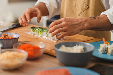 Obraz na płótnie Canvas Sushi preparation close up on a male chief's hands rolling vegan roll. Vegan menu