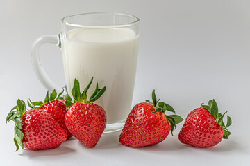 glass mug of milk and sweet fragrant strawberries on a white surface