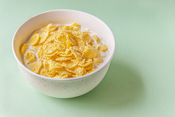 cornflakes with milk in a ceramic bowl on a light green surface