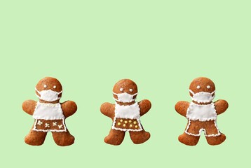 Cute gingerbread family with protective face masks, isolated, green background. Greeting card, copy space for text. Creative concept in coronavirus (COVID-19) time