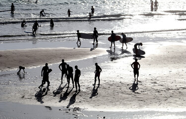 Fototapeta na wymiar siluetas al atardecer en la playa con tablas de surf