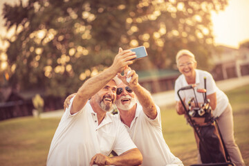 Senior golfers using phone and taking self portrait. Focus is on foreground.  Our best photo.