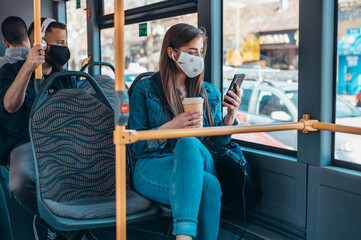 Woman wearing protective mask riding a bus while using a smartphone