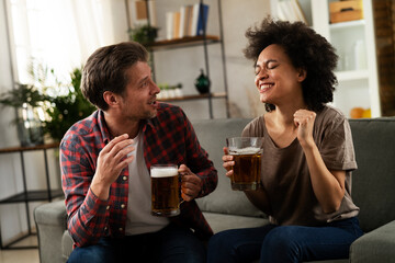 Boyfriend and girlfriend drinking beer at home. Happy couple watching sports game on tv..