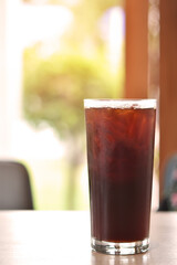 Vertical view, Iced black coffee in tall glass on wooden table.