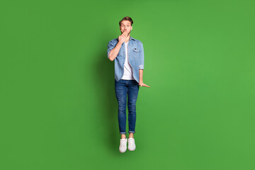 Full length body size photo of young guy jumping high shut mouth with palm isolated bright green...