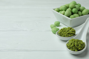 Tasty wasabi nuts and sauce on white wooden background