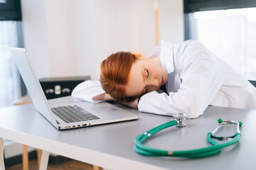 Close-up face of tired exhausted overworked young female doctor in white coat sleeping lying at...