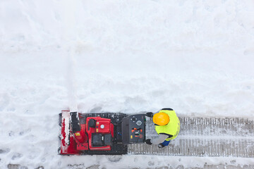 Worker cleaning snow on the sidewalk with a snowblower. Wintertime