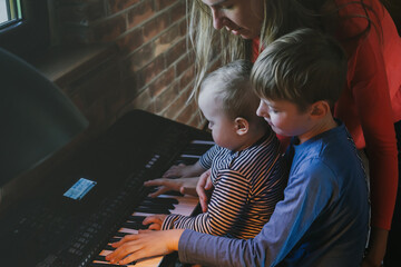 Emotional family picture. Mother and two little sons, boys, brothers, siblings. Mom care when eight years old son playing piano with his cute little brother.