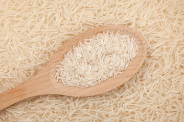 Rice in a wooden spoon, close-up. Background of white vermicelli or raw Japanese rice flour noodles. Gluten-free products