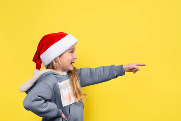 Little beautiful girl in red santa hat smiling and pointing her finger.