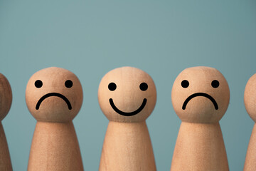 Wooden figure smile between sadness on blue background , Emotion selection and lifestyle concept.