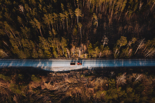Aerial view of tractor with cargo trailer on the sun illuminated forest road in Lithuania, Sveicarija, Kaunas, Lithuania.