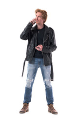 Attentive young biker or rocker redhead male listening cell phone call looking away. Full body length isolated on white background