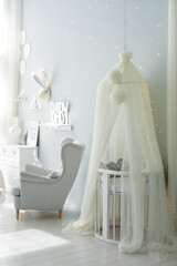 Stylish scandinavian interior of newborn baby room with bed and grey armchair. Hanging white canopy with cradle. Decor children room with furniture. Crib in a modern nursery room. Baby cot with canopy