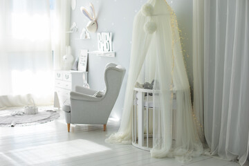 Stylish scandinavian interior of newborn baby room with bed and grey armchair. Hanging white canopy with cradle. Decor children room with furniture. Crib in a modern nursery room. Baby cot with canopy © stock_studio