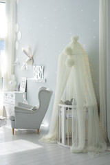 Stylish scandinavian interior of newborn baby room with bed and grey armchair. Hanging white canopy with cradle. Decor children room with furniture. Crib in a modern nursery room. Baby cot with canopy