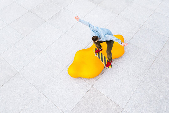 Aerial view of professional skateboarder jumping over the modern yellow object in urban skate park in Kaunas, Lithuania.