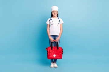 Full length body size photo of little female doctor working in ambulance smiling keeping red bag isolated on bright blue color background