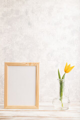 Wooden frame with orange tulip flower in glass on gray concrete background. side view, copy space, mockup.