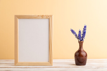 Wooden frame with blue muscari hyacinth flowers in ceramic vase on orange pastel background. side view, copy space, mockup.