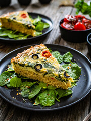Millet quiche with spinach, black olives, cherry tomatoes and ricotta on wooden table 