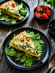 Millet quiche with spinach, black olives, cherry tomatoes and ricotta on wooden table 