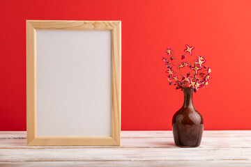 Wooden frame with purple barrenwort flowers in ceramic vase on red pastel background. side view, copy space, mockup.