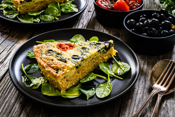 Millet quiche with spinach, black olives, cherry tomatoes and ricotta on wooden table 