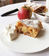 Stück Apfelstrudel mit Rosinen und Puderzucker bestäubt auf weiße, Teller mit Sahne, Schlagobers, Spezialität aus Österreich und Südtirol, Alto Adige