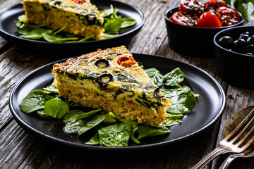 Millet quiche with spinach, black olives, cherry tomatoes and ricotta on wooden table 