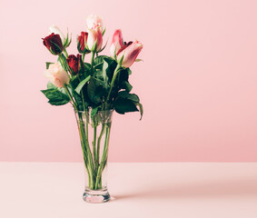 Beautiful fresh roses in glass vase are arranged on table against a pastel pink background. Selective focus copy space