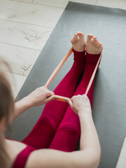 Resistance band exercise at home. Woman doing pilates workout using elastic strap pulling with arms for shoulder training on yoga mat indoors. Sport and healthy active lifestyle concept. - obrazy, fototapety, plakaty