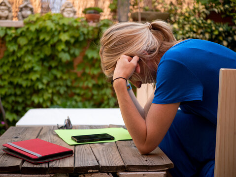 Adult Depressed Blonde Woman Hunched Over Her Hands Sitting In The Garden