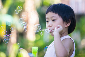 A boy is blowing many bubbles in the air over a green garden background.