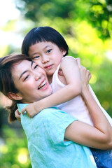 Asian mother is smiling while holding her son up over a green garden background. Quality family time concept.