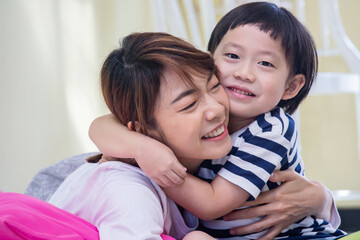 Asian boy is smiling, looking at camera and hugging his mother with love. Quality family time concept.