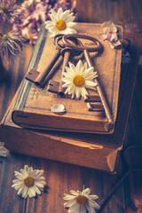 Key to knowledge concept. Old keys on a vintage book with flowers on wooden background