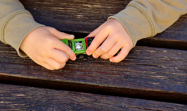Children's hands with toy cars on a wooden background. A child plays with a children's model car.