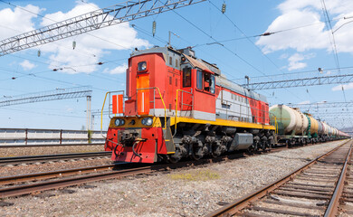 Fototapeta na wymiar Freight locomotive pulls train with fuel tanks against blue sky.