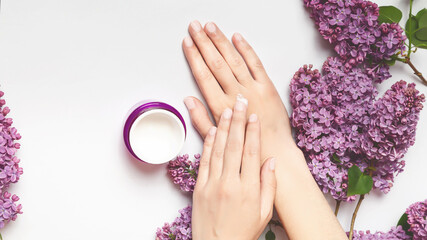 Natural cosmetics for women from lilac flowers and petals. Woman applying organic moisturizer to hands. Hand skin care concept