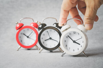 white analog alarm clock with blurred red and black and human's hand on grunge grey background ,...