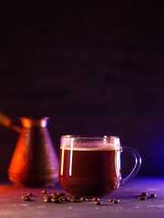 Glass cup of hot freshly brewed coffee , dark background with colored lighting. Turkish coffee, cezva
