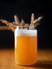 Stylish creative glass of unfiltered wheat beer and wheat ears, black background, vertical photo