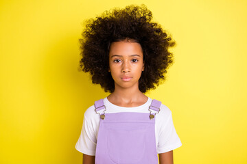 Photo of calm adorable little girl curly hairstyle look camera wear purple overall isolated yellow...