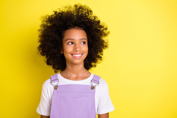 Portrait of optimistic cute curly girl wear white t-shirt look empty space isolated on yellow color...