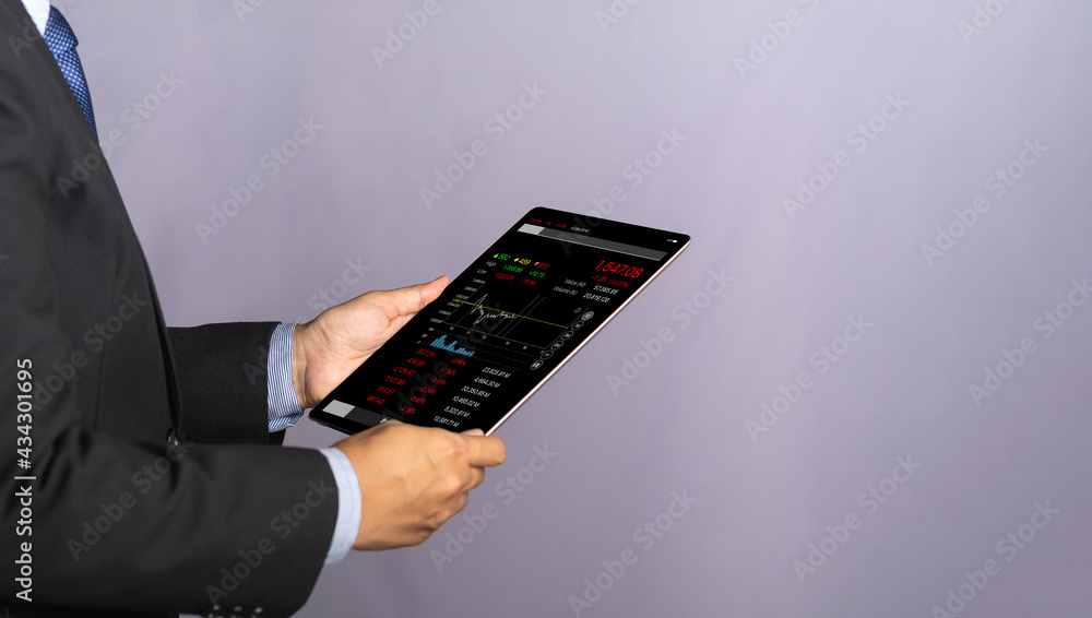 Poster side view of a businessman holding and reading business graphs and stock charts on a digital tablet.